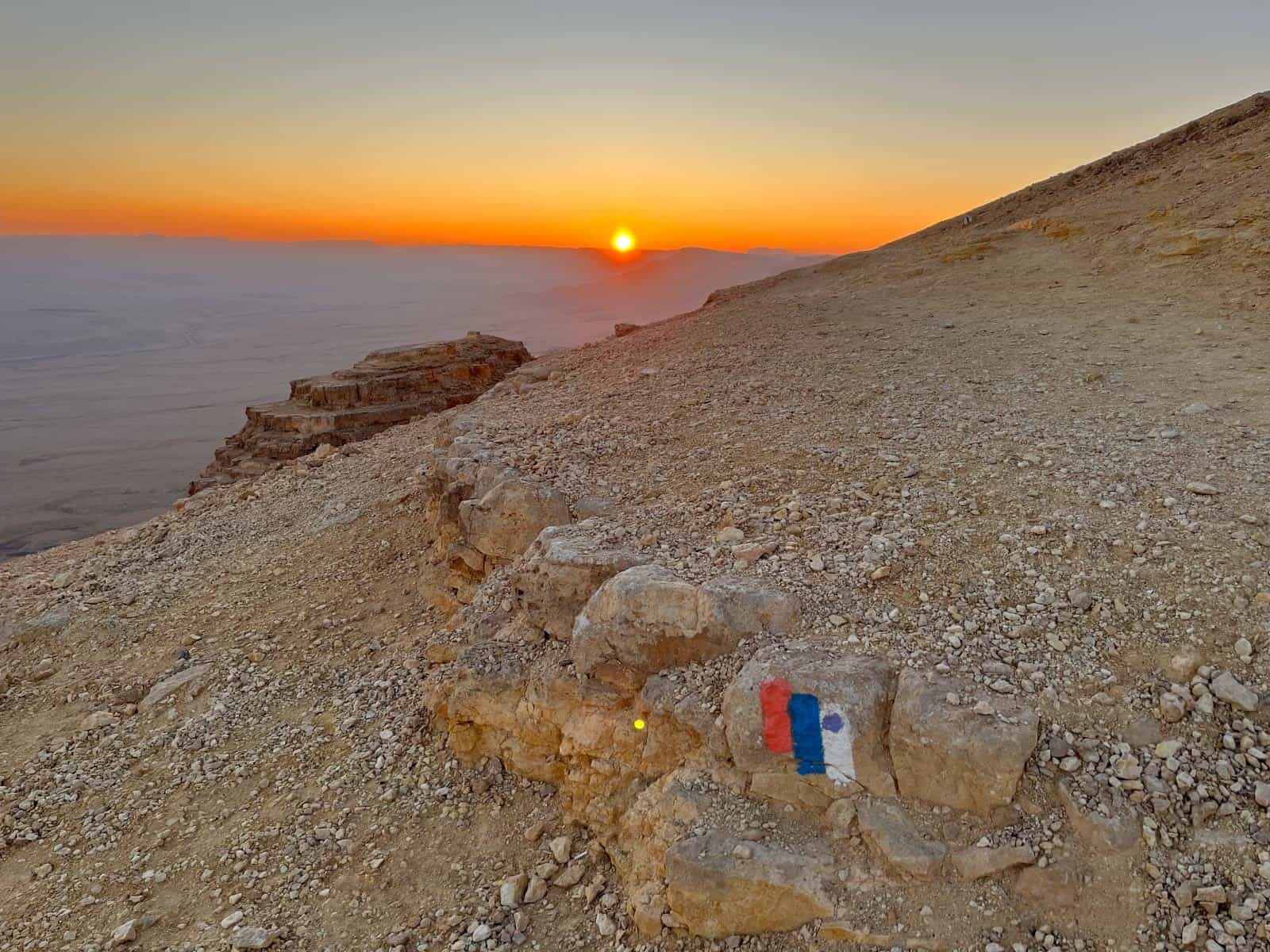 The sun is setting over a mountain with a flag on it.