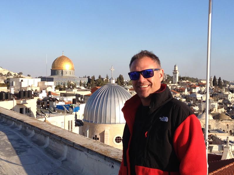 Jonathan Cutler standing on a rooftop with a view of the city of Jerusalem.