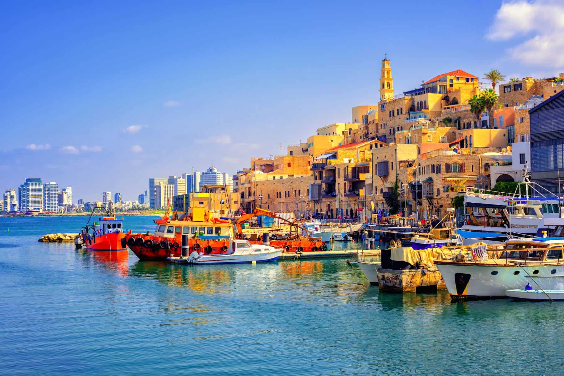 Vibrant harbor with boats in front of old city buildings and modern skyline in the background.