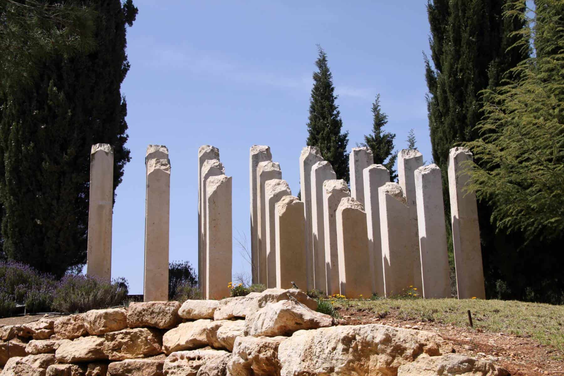 Row of standing stone columns amid vegetation under a clear blue sky.