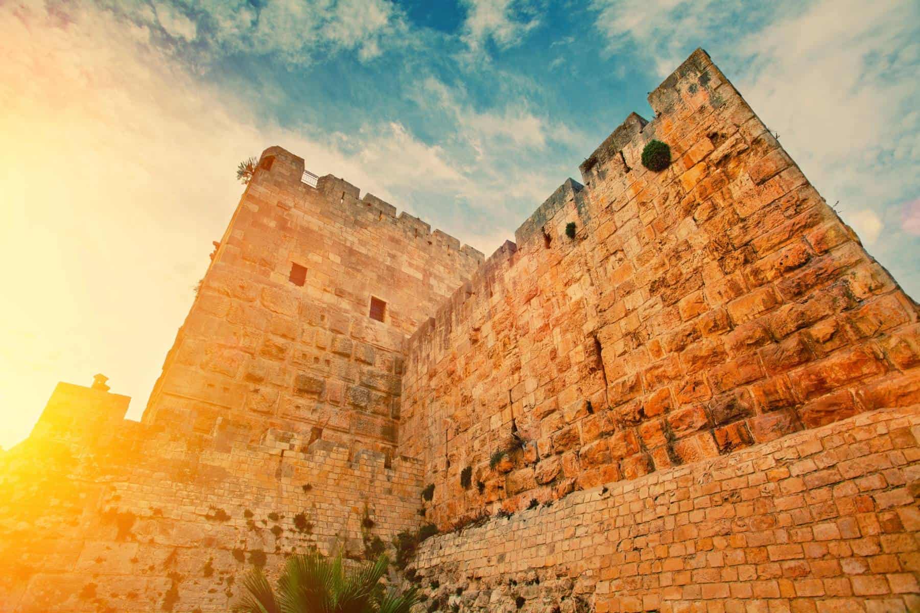 Ancient fortress walls bathed in warm sunlight against a blue sky with clouds.